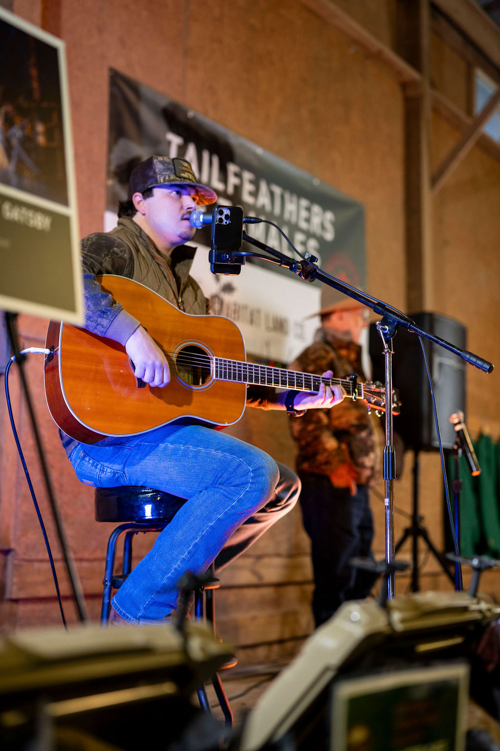 Performer playing guitar and singing on stage while sitting on a black stool
